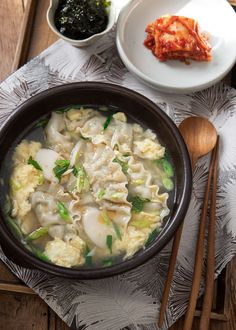 a bowl filled with dumplings and vegetables next to chopsticks on a table