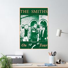 the smiths on tour poster hanging on a wall above a desk with a plant