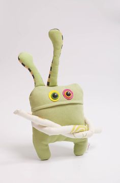 a green stuffed animal with big eyes holding a stick