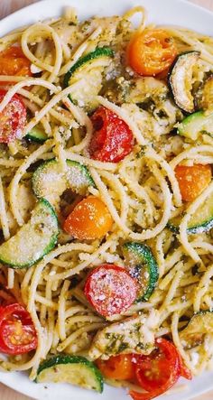 pasta with zucchini, tomatoes and other vegetables in a white bowl on a wooden table