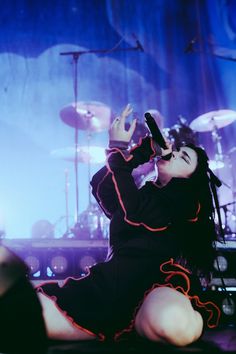 a woman sitting on the ground in front of a stage with drums and microphones