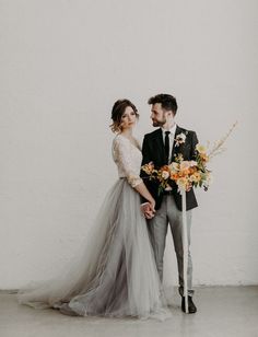 a bride and groom standing next to each other in front of a white wall holding an umbrella