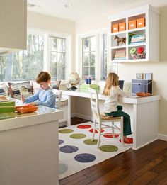 two children sitting at a desk in a room with lots of windows and white furniture