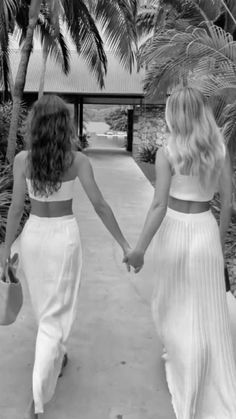 two women walking down a path holding hands and wearing white dresses with matching crop tops