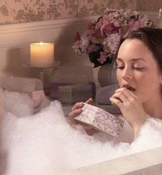 a woman sitting in a bathtub with soap on her face and holding a box