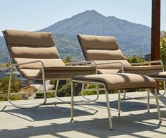 three lounge chairs sitting next to each other on top of a cement patio with mountains in the background