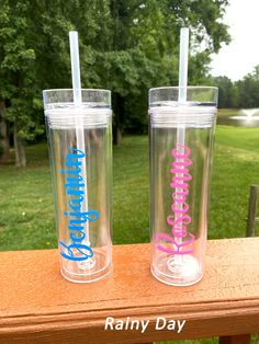 two personalized tumblers sitting on top of a wooden table with trees in the background