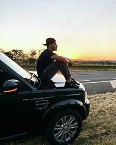 a man sitting on the hood of a car in front of a highway at sunset