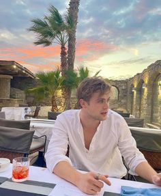 a man sitting at a table in front of a palm tree and looking off into the distance