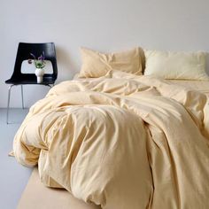 an unmade bed in a white room with a black chair and vase on the floor