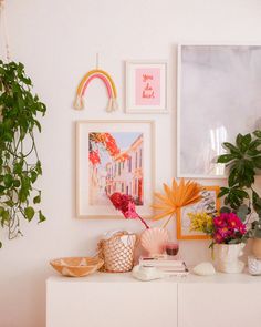 a white dresser topped with lots of vases filled with flowers next to pictures on the wall