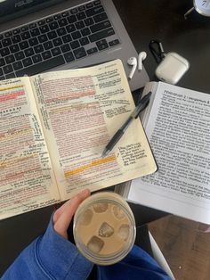 a person holding a coffee cup in front of an open book on a laptop computer