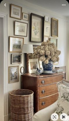 a living room with pictures on the wall and a vase full of flowers sitting on top of a dresser