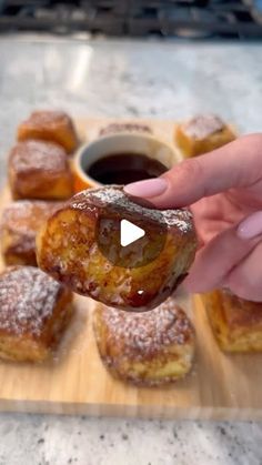 a person is holding up a doughnut in front of other pastries on a cutting board