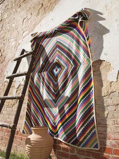 a crocheted blanket hanging on a brick wall next to a vase and ladder