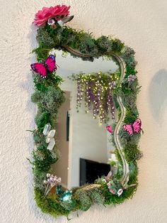 a mirror that has some flowers and grass on it, hanging from the side of a wall