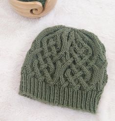 a green knitted hat sitting on top of a white blanket next to a wooden bowl