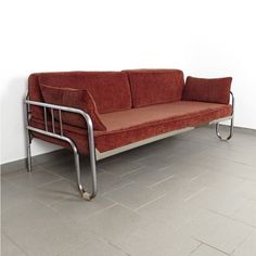 a red couch sitting on top of a metal frame next to a white wall in an empty room