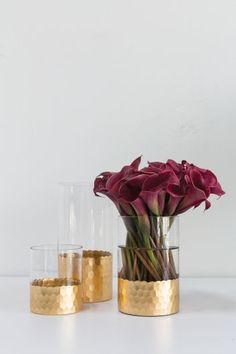 three vases with flowers in them sitting on a table next to each other and gold rimmed glasses