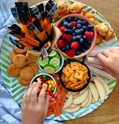 a person holding their hand over a platter of fruit and snacks