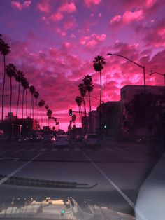 the sun is setting behind palm trees and cars are driving down the street in front of them