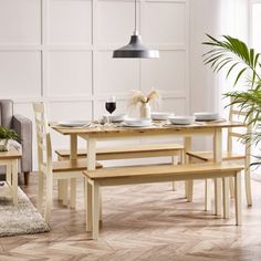 a dining table and bench in a room with white walls, wood flooring and large potted plant