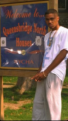 a young man standing in front of a welcome to queensbridge north house sign on the grass