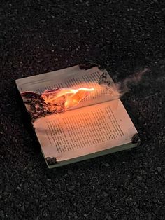 an open book sitting on top of a black ground next to a lit fire pit