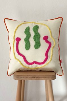 a white pillow with green and pink designs on it sitting on a wooden stool next to a wall