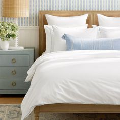 a bed with white linens and blue pillows in a small room next to a nightstand