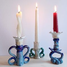 three candles are sitting next to each other in blue and white vases with handles