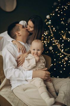 a man and woman holding a baby in front of a christmas tree