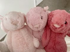 two pink and one white stuffed animals sitting next to each other on top of a bed