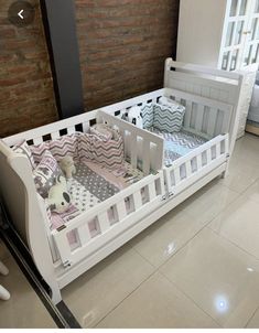 a white crib with pink and gray bedding in a room next to a brick wall