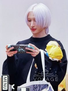 a woman with white hair is holding a cell phone and looking at the screen while wearing a black sweater