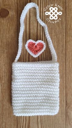 a crocheted white bag with a red heart on the front and bottom, sitting on a wooden surface