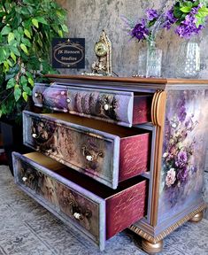 an ornate dresser with flowers painted on the front and drawers, is next to a potted plant