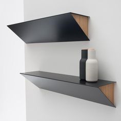 two black shelves on the wall with one shelf holding a vase, and another shelf above it