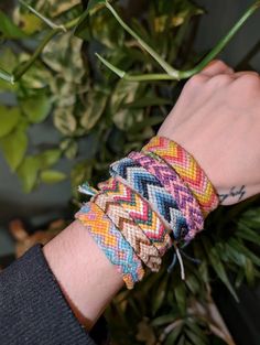 a person wearing two different colored bracelets on their wrist next to a plant with green leaves