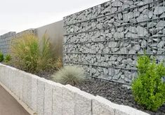 the stone and steel fence is next to some plants