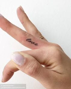 a person's hand with a small tattoo on the middle finger that says love