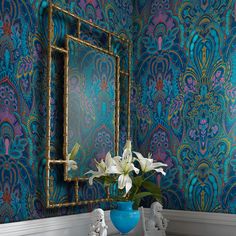 a blue vase with white flowers in front of a mirror on a wallpapered room