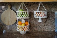 two hanging baskets filled with fruit sitting on top of a counter next to a cutting board