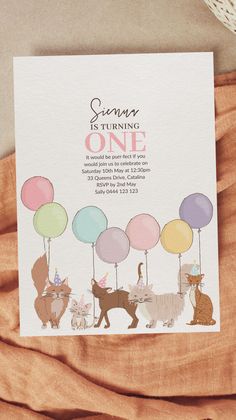 a birthday card with cats and balloons on it, sitting next to a pile of blankets