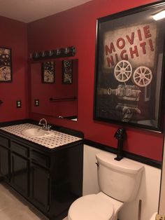 a white toilet sitting next to a bathroom sink under a framed movie poster on the wall