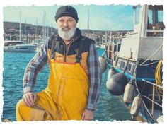 an old man with a beard and wearing overalls standing in front of a boat