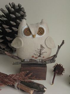 an owl figurine sitting on top of a piece of wood next to pine cones