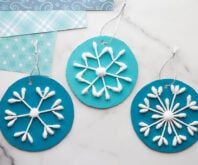 three snowflakes are hanging from strings on a table with blue and white paper