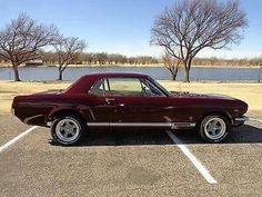 a maroon car parked in a parking lot next to some trees and water on a sunny day