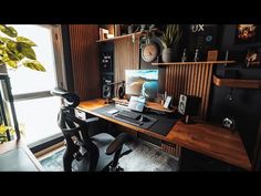 a desk with a computer on top of it in front of a window and some plants